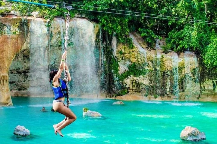 A guest swinging over a turquoise pool below a waterfall