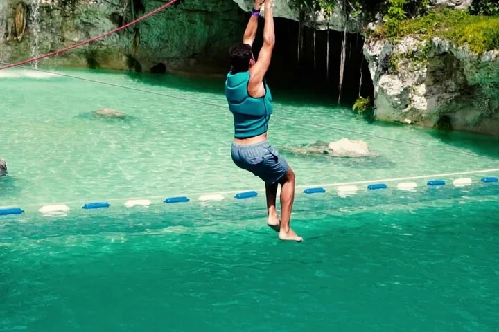A zipline rider about to splash into a turquoise lagoon